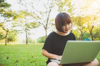 young asian womans legs on the green grass with open laptop girls hands on keyboard